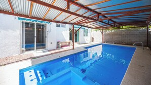 A residential swimming pool with a metal roof structure and a white exterior wall. - Cozy Cool 3 Bedrooms Home W~Pool (North Las Vegas)