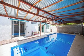 A residential swimming pool with a metal roof structure and a white exterior wall. - Cozy Cool 3 Bedrooms Home W~Pool (North Las Vegas)