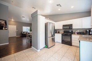 A modern kitchen with stainless steel appliances, white cabinetry, and a granite countertop. - Cozy Cool 3 Bedrooms Home W~Pool (North Las Vegas)