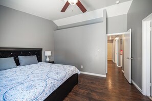Un dormitorio con cama, mesita de noche y lámpara. Se ve un pasillo que conduce a otra habitación.