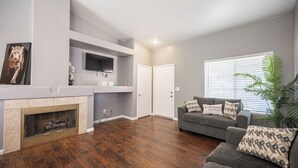A living room with a fireplace, a grey couch with patterned cushions, and a television mounted on the wall. - Cozy Cool 3 Bedrooms Home W~Pool (North Las Vegas)