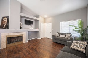 A living room with a fireplace, a grey couch with patterned cushions, and a television mounted on the wall. - Cozy Cool 3 Bedrooms Home W~Pool (North Las Vegas)
