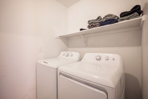 A laundry room with two white front-loading washing machines and a shelf above holding folded towels. - Cozy Cool 3 Bedrooms Home W~Pool (North Las Vegas)