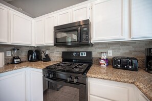A kitchen with white cabinets, a black stove, a microwave, and a toaster. - Cozy Cool 3 Bedrooms Home W~Pool (North Las Vegas)