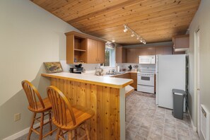 A kitchen with wooden cabinets, a white countertop, a bar stool, and a microwave. - New Listing! Explore Big Sky, Hike + Ski (Big Sky)