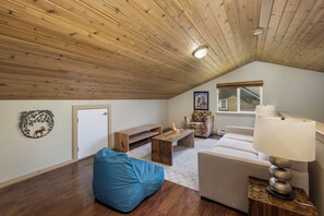 Habitación estilo loft con techo inclinado, un banco de madera, un sillón orejero azul, un sofá blanco y una lámpara sobre una mesita.