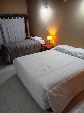 Una habitación de hotel con dos camas, una mesita de noche con una lámpara y una cortina.