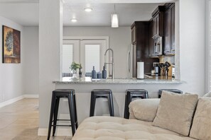 A modern kitchen with a central island, bar stools, and a seating area with a sofa. - Figaro - A Birdy Vacation Rental (San Antonio)