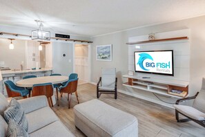 Ein modernes Wohnzimmer mit Essbereich, einem an der Wand montierten Fernseher und einer Küche im Hintergrund.