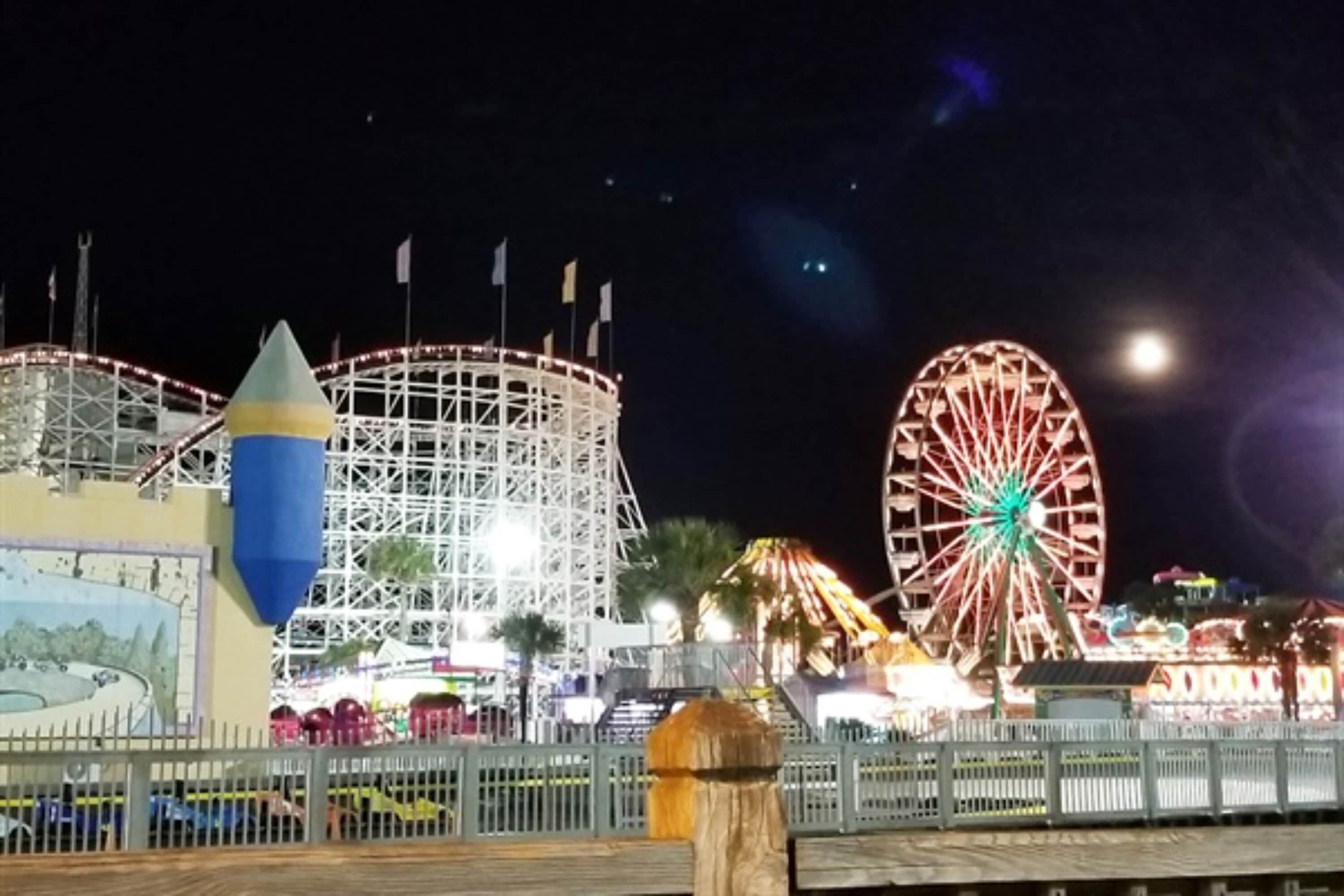 Parque de atracciones nocturno con noria y montañas rusas.