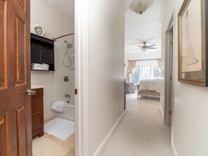 Ein Flur, der zu einem Schlafzimmer führt, mit Deckenventilator, Dusche und Badewanne.