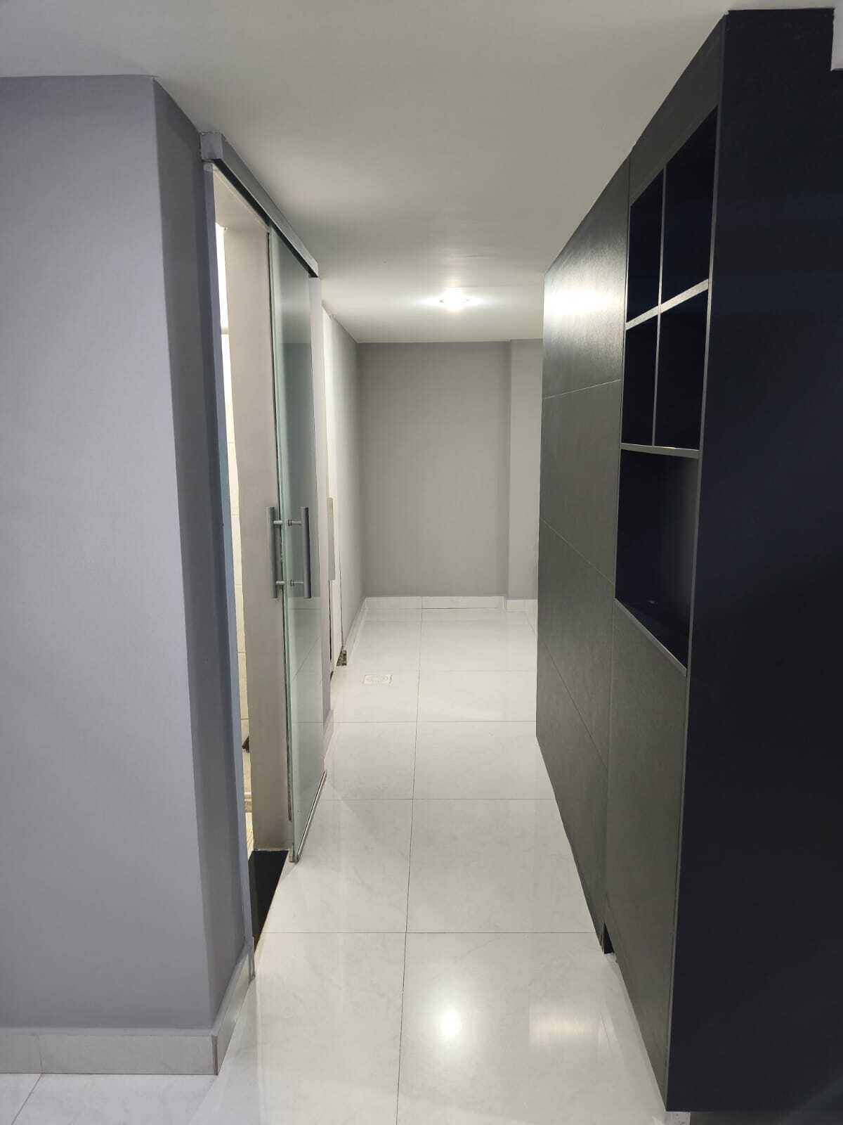 A hallway with a glass door, a tiled floor, and a dark-colored wall.