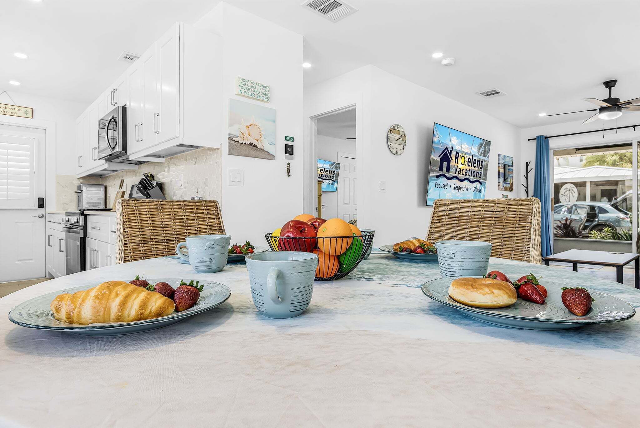 Una cocina moderna con muebles blancos, una mesa de comedor dispuesta con platos de comida y un cartel de Roelens Vacations.