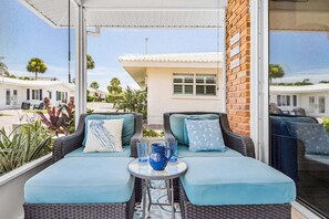 A balcony with wicker furniture, a table with a pitcher and glasses, and a view of a building with a tiled roof. - Beachside Escape with Pool & Steps to Crescent Beach - Aloha Kai #51 (Siesta Key)