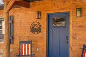 A wooden cabin with a blue door, a number sign, a mountain and bear logo, and a bench. - Resort Cabin: Lazy River, Pickleball, Pools (Hollister)