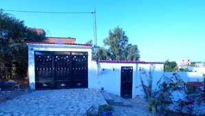 Un edificio blanco con tejado de tejas rojas, una verja negra y un acceso empedrado de piedra.