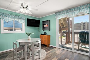 A room with a dining table, chairs, a TV, a wooden cabinet, and a sliding glass door leading to an outdoor area. - Cozy Ocean Block Condo | Walk to Beach (Ocean City)