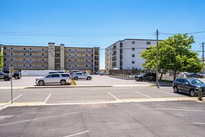 A parking lot with several cars, a building with balconies, and a tree. - Cozy Ocean Block Condo | Walk to Beach (Ocean City)