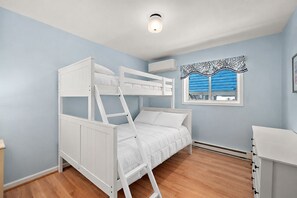 A bunk bed room with a window, a dresser, and a ceiling light. - Cozy Ocean Block Condo | Walk to Beach (Ocean City)