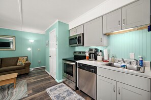 A compact kitchen with a dishwasher, stove, microwave, and a coffee maker. - Cozy Ocean Block Condo | Walk to Beach (Ocean City)