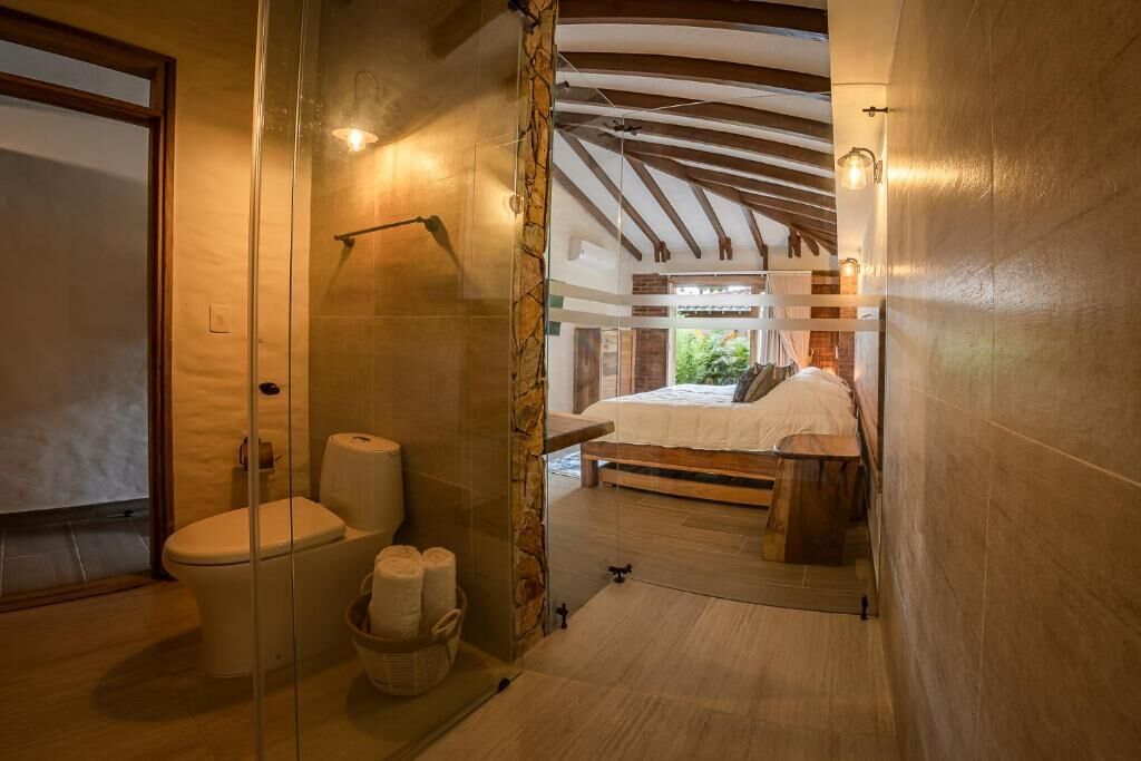 Un baño con cabina de ducha de vidrio, inodoro y cama con cabecero de madera.