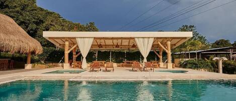 A pool with lounge chairs and a covered seating area.