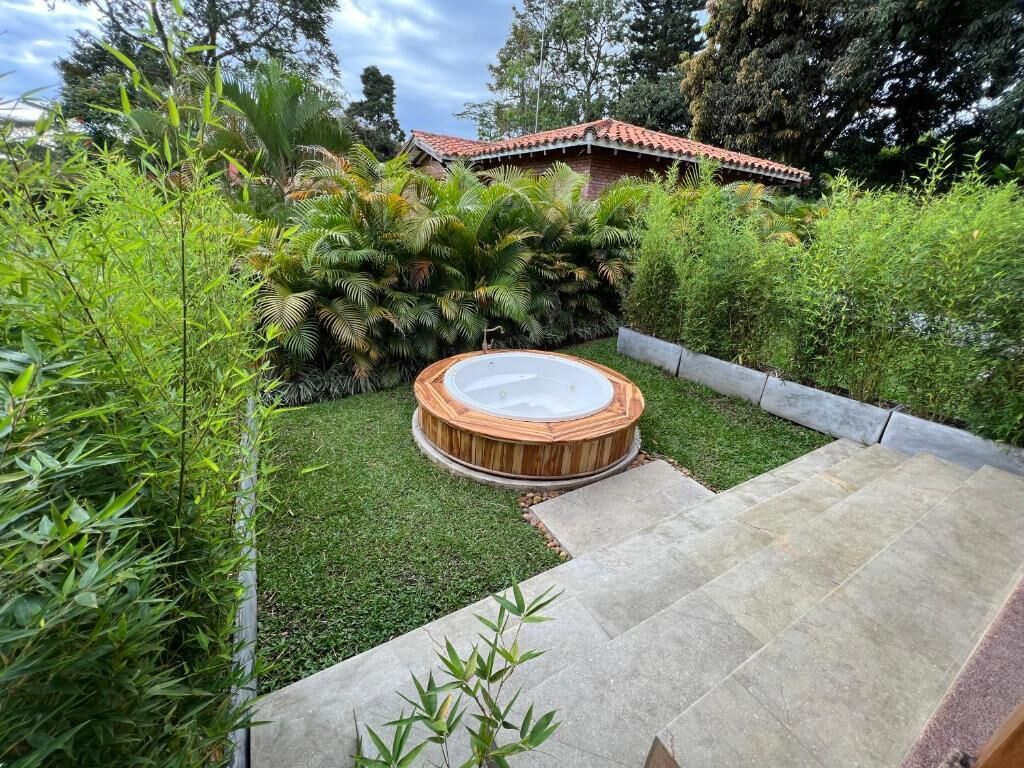 Un jacuzzi en un jardín con patio empedrado y abundante vegetación.