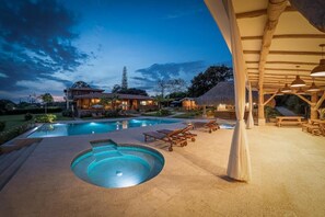 A swimming pool with lounge chairs and a covered area, surrounded by buildings and trees.