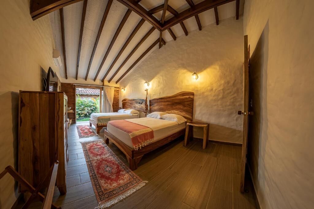 Un dormitorio con techo de madera, una cama con cabecera, mesitas de noche y una alfombra roja estampada.