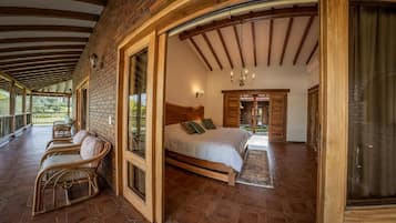 A bedroom with a wooden bed, a sitting area with chairs, and a view of the outdoors.
