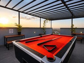 Ein Billardtisch mit Spielstöcken, einer roten Filzoberfläche und Blick auf die Stadt im Abendrot.