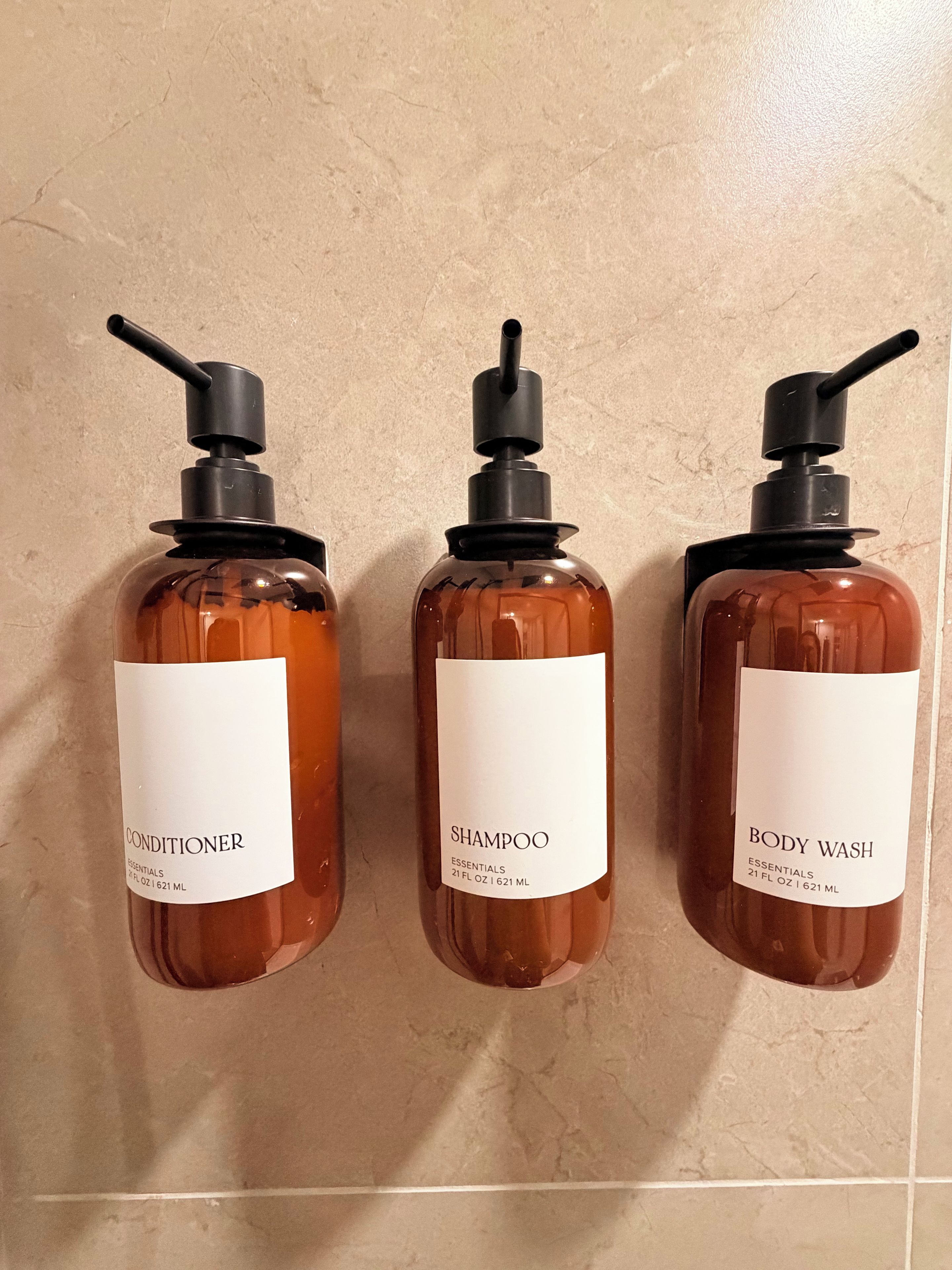 Three bottles of toiletries on a tiled wall.