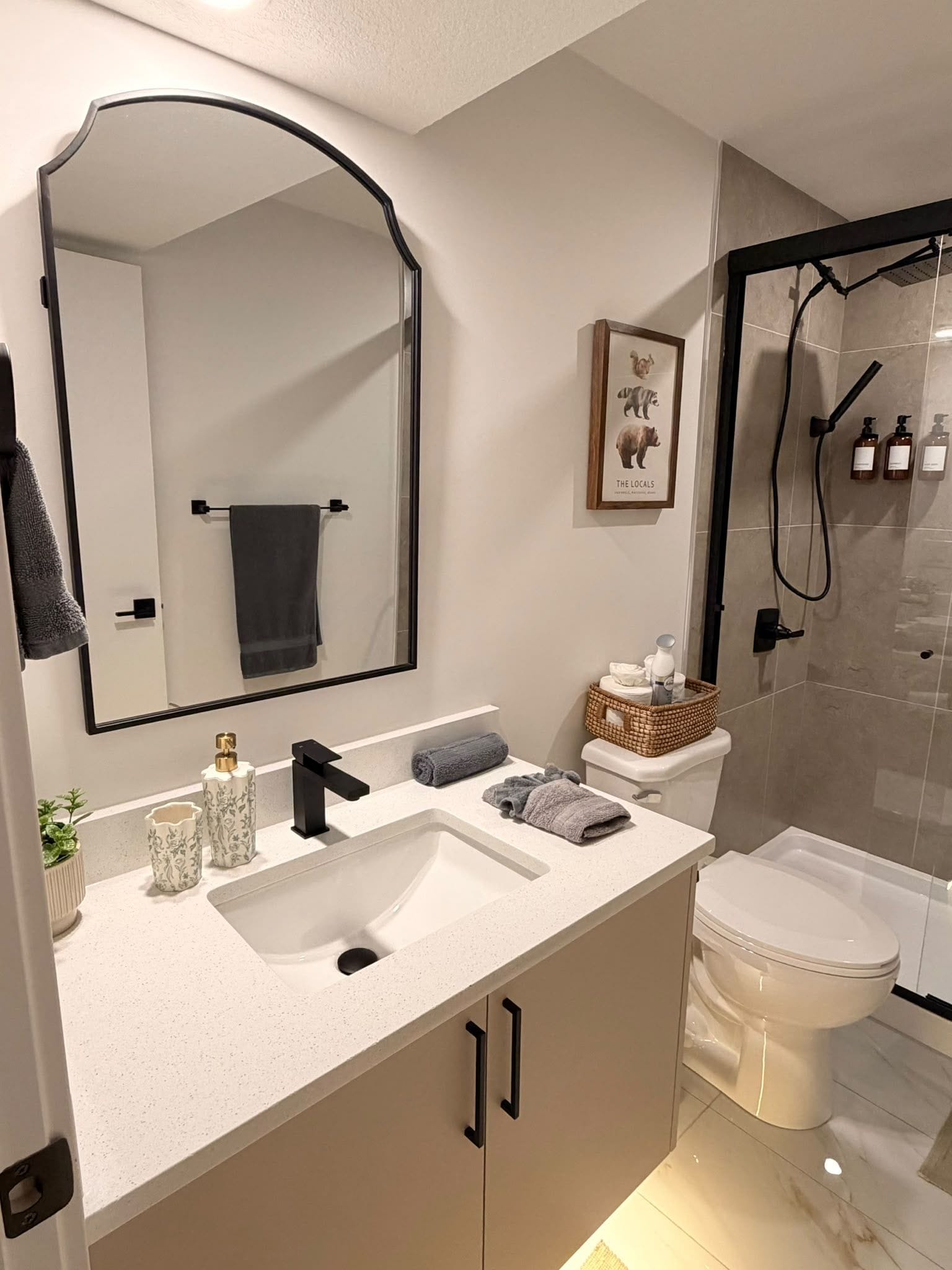 A modern bathroom with a large mirror, a sink with two faucets, a toilet, and a shower area.
