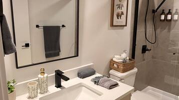 A modern bathroom with a large mirror, a sink with two faucets, a toilet, and a shower area.