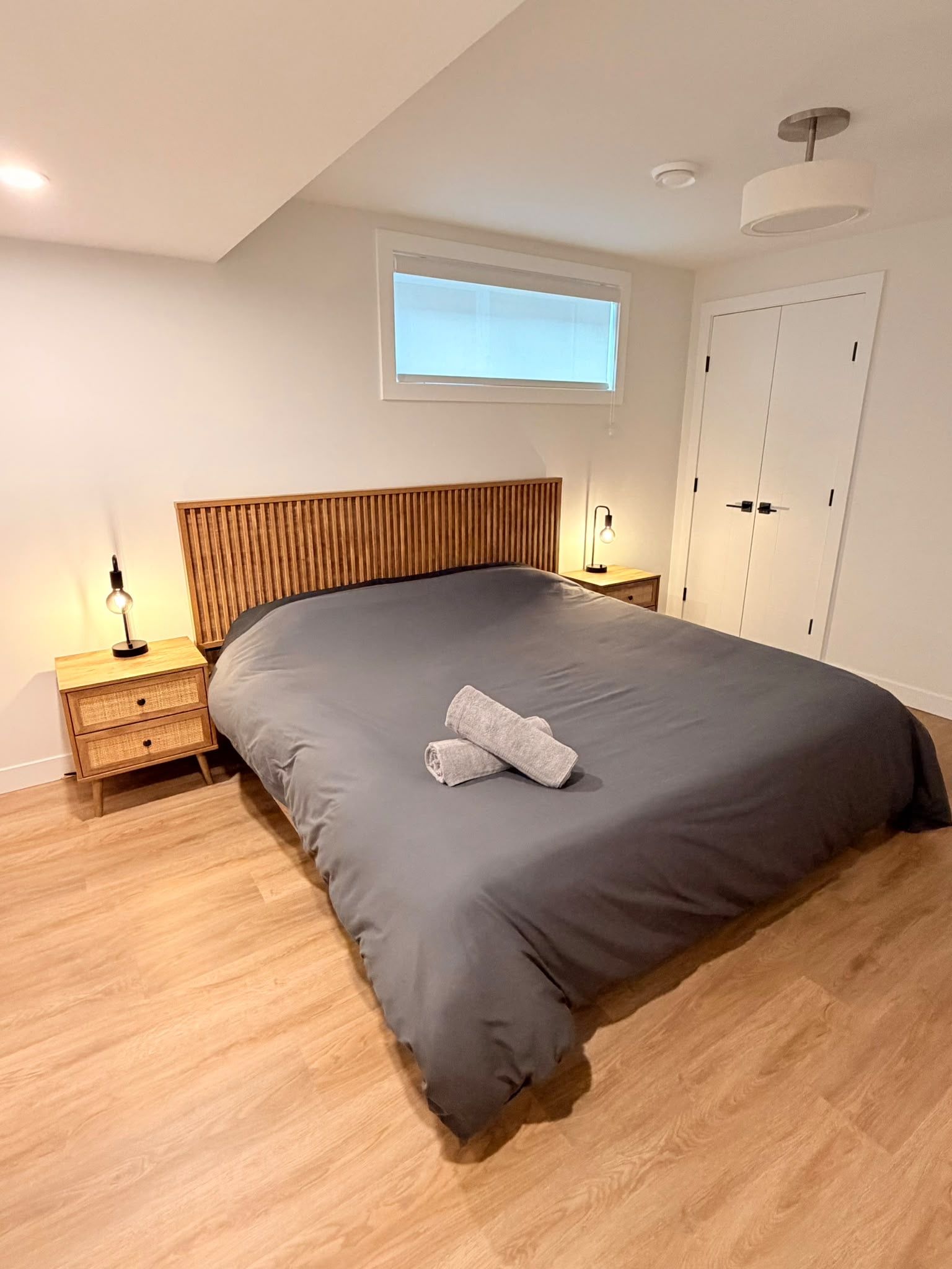 A bedroom with a large bed, wooden headboard, two bedside tables with lamps, a window, and a wardrobe.