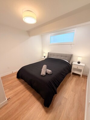 A bedroom with a bed, a window, a nightstand, and a lamp.