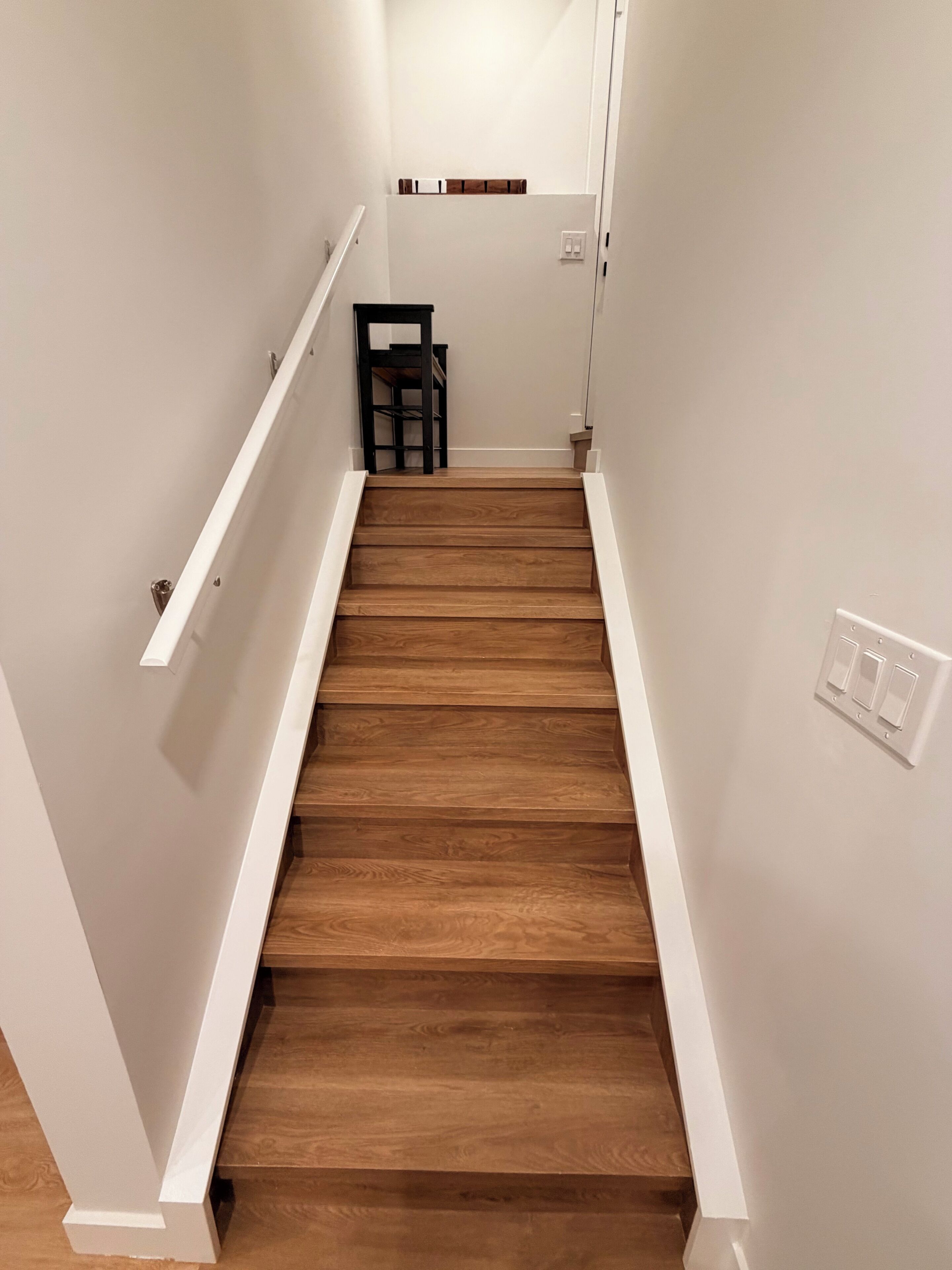 A wooden staircase with white walls and a handrail.