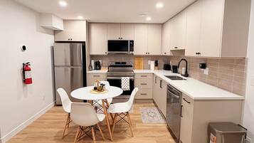 Una cocina moderna con armarios blancos, electrodomésticos de acero inoxidable y una mesa redonda con sillas.