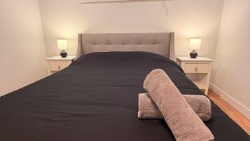 A bedroom with a large bed, two bedside tables with lamps, a window with blinds, and a ceiling light.