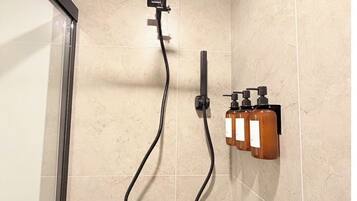 Una doccia con un pannello quadrato a soffitto, un soffione a mano, un getto doccia manuale e un dispenser di sapone fissato alla parete.