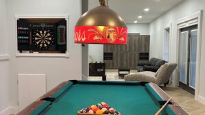 Uma mesa de bilhar com taco, um alvo de dardos e um suporte para bolas de bilhar.
