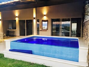 Ein Pool mit Fliesen umgeben, eine Bar mit Hockern und Blick auf die Landschaft durch große Schiebetüren.