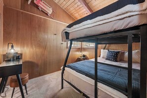Ein Stockbett mit Schreibtisch und Stuhl, eine Lampe sowie ein kleiner Tisch ebenfalls mit Lampe.