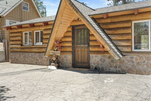 Eine Blockhütte mit steinernen Fundamenten, einer Holztür und einem Willkommen-Schild.