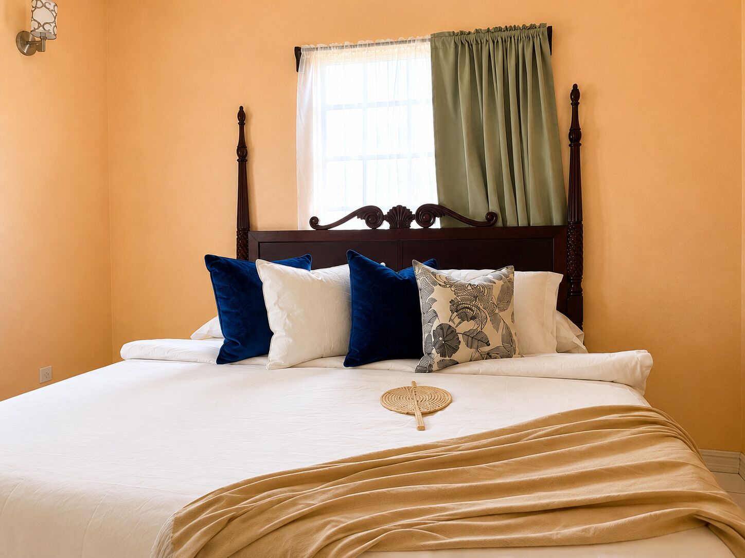 Un lit avec une tête de lit en bois, une literie blanche, des coussins bleus à motifs, un plaid beige et une fenêtre avec un rideau vert.