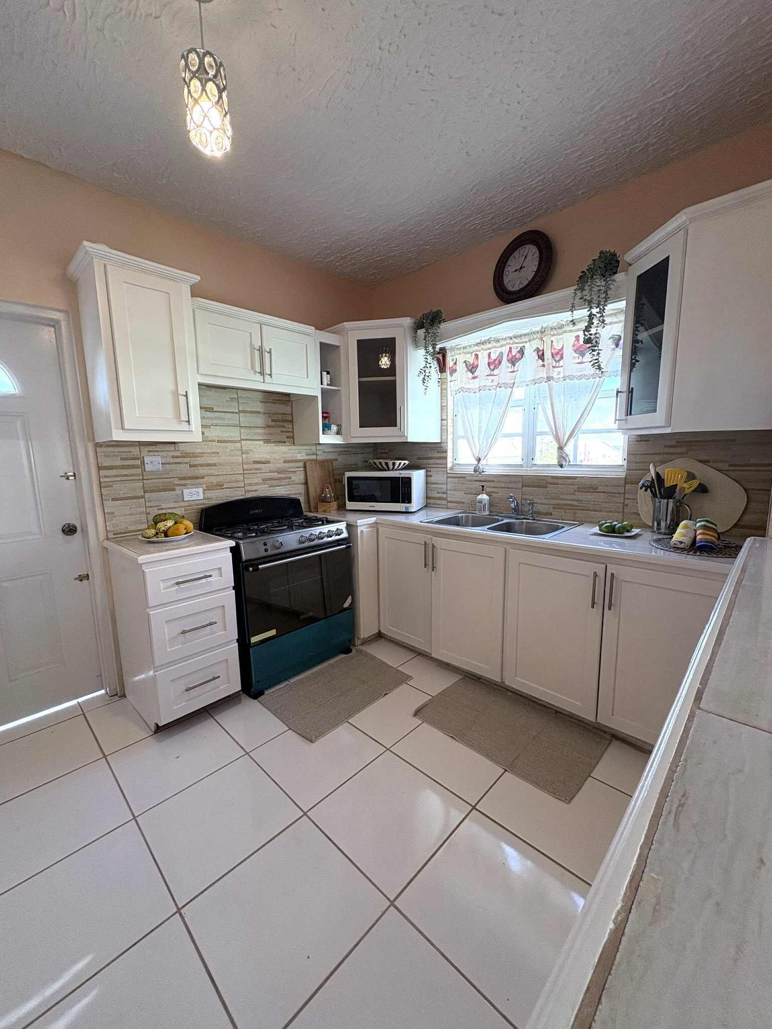 A kitchen with white cabinets, a stove, a microwave, and a sink.