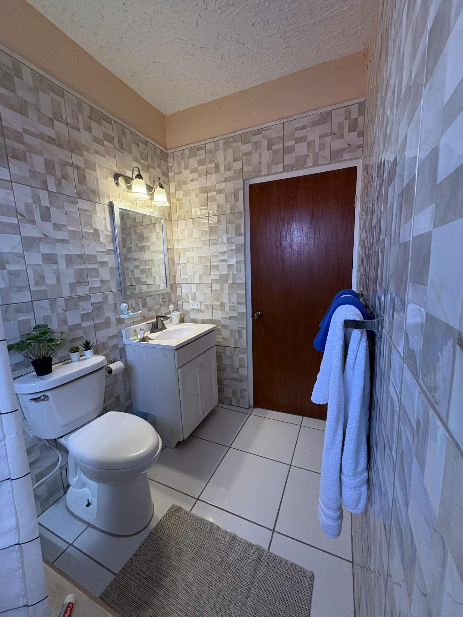 A bathroom with a toilet, sink, and mirror, tiled walls, and a towel rack.