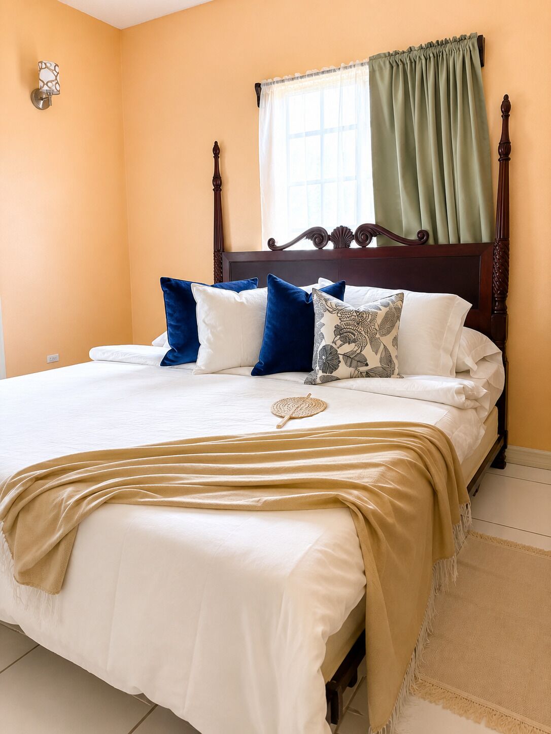 A bed with a wooden headboard, white bedding, and multiple pillows in a room with yellow walls and a window with green curtains.