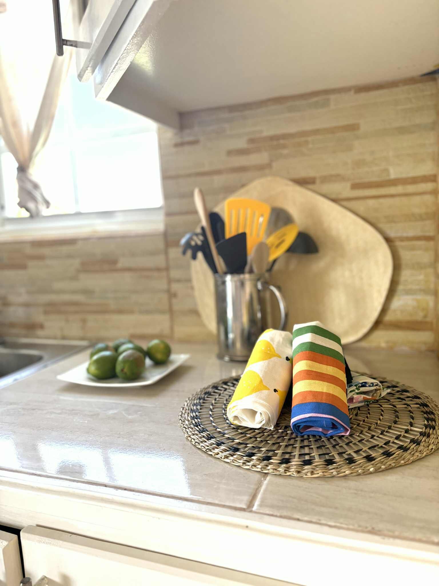 Un piano di lavoro in cucina con un sottobicchiere intrecciato, un piatto di lime e asciugamani arrotolati.