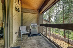 Eine überdachte Veranda mit Grill, Stuhl und Blick auf einen Wald.
